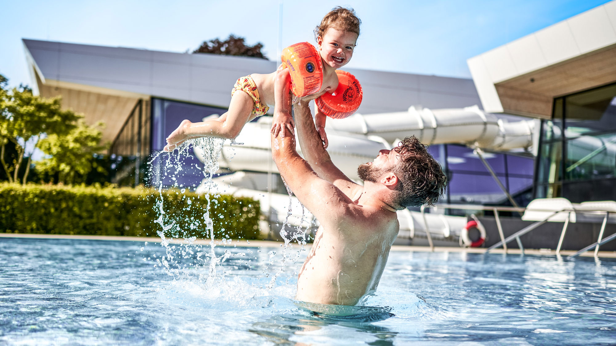 Vater hält Kind im Wasser hoch in die Luft